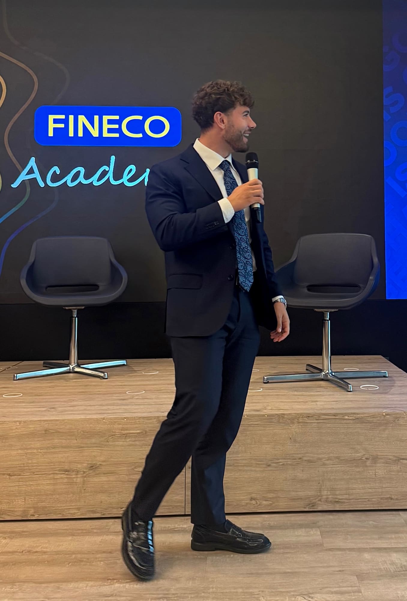 Simone Spongano sul palco del Fineco Academy, microfono in mano, davanti all'insegna luminosa FINECO Academy